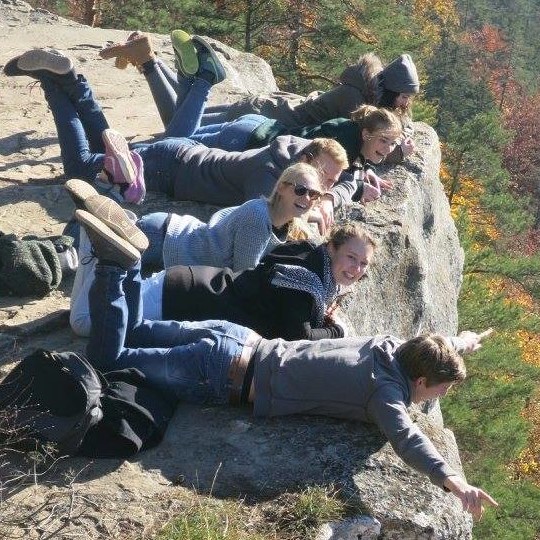 Group of six students on a ledge looking down at fall colors, pretending to be flying